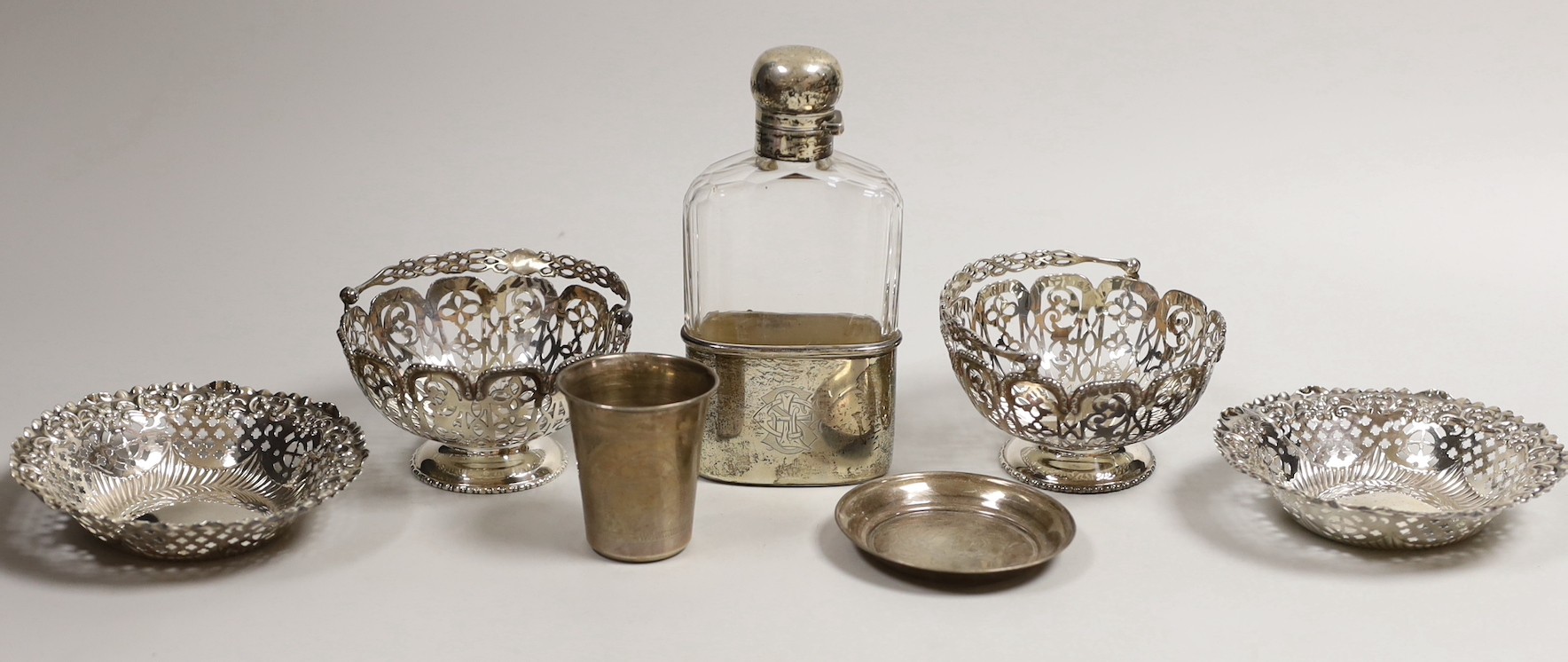 A pair of Edwardian pierced silver bonbon baskets, Nathan & Hayes, Birmingham, 1909, diameter 10.1cm, a pair of silver bonbon dishes, an Edwardian silver mounted glass hip flask, by Charles & George Asprey, London, 1908